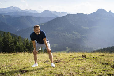 Müder Mann mit Händen auf den Knien in den Bergen an einem sonnigen Tag - DIGF16358