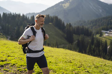 Lächelnder Mann mit Rucksack beim Wandern auf einem Berg - DIGF16363