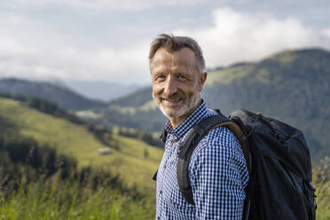 Lächelnder männlicher Wanderer mit Rucksack auf einem Berg - DIGF16366