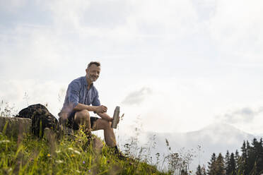 Smiling man with insulated drink container sitting on mountain - DIGF16371