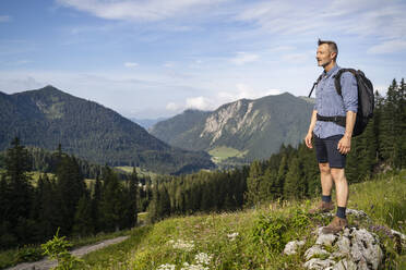 Männlicher Wanderer mit Rucksack, der die malerische Landschaft vom Berg aus betrachtet - DIGF16375