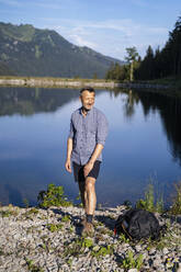 Smiling man standing at lakeshore on sunny day - DIGF16381