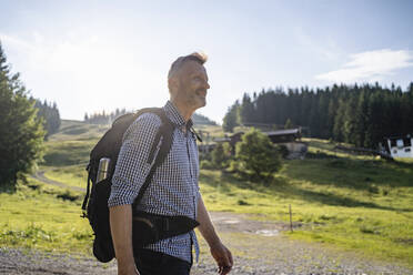 Lächelnder männlicher Rucksacktourist beim Wandern an einem sonnigen Tag - DIGF16384