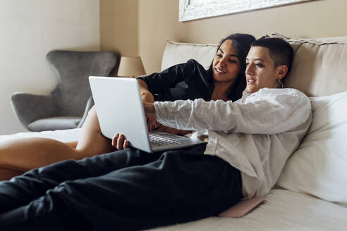 Lesben teilen sich einen Laptop, während sie zu Hause auf dem Bett liegen - MEUF04075
