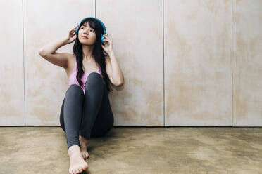 Young woman listening music through headphones while sitting on floor - ASGF01102