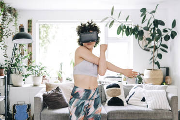 Junge Frau mit Virtual-Reality-Headset beim Stretching zu Hause - ASGF01110