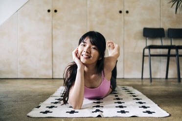 Smiling woman exercising while lying on blanket - ASGF01115