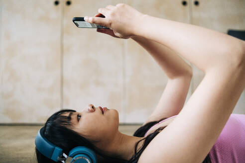 Junge Frau hört Musik über Kopfhörer, während sie zu Hause ein Mobiltelefon benutzt - ASGF01118