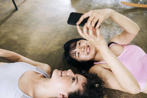 Frau, die ein Selfie mit ihrem Smartphone macht, während sie mit ihrer Freundin auf dem Boden liegt - ASGF01120