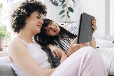 Female friends sharing digital tablet while sitting in living room - ASGF01143