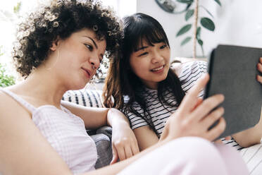 Smiling woman using digital tablet with female friend at home - ASGF01144