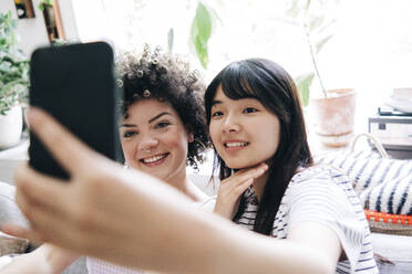 Lächelnde Freundinnen machen ein Selfie mit dem Handy zu Hause - ASGF01147