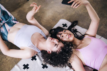 Lächelnde Frau nimmt Selfie mit weiblichen Freund durch Smartphone zu Hause - ASGF01175