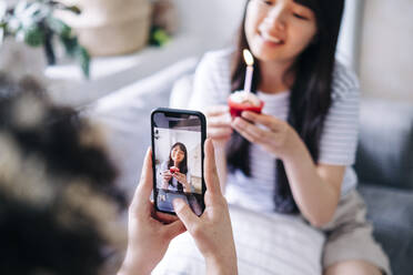 Frau fotografiert Freundin mit Muffin in der Hand mit dem Smartphone zu Hause - ASGF01177