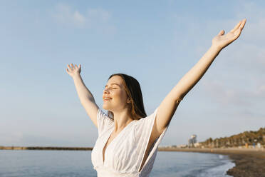 Smiling woman with arms outstretched standing at beach - XLGF02199