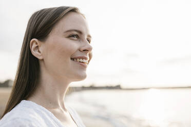 Smiling beautiful young woman looking away at beach - XLGF02204