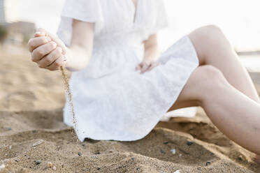 Frau spielt mit Sand, während sie am Strand sitzt - XLGF02208