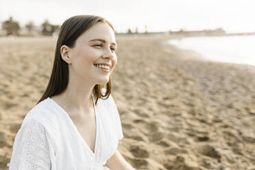 Smiling young woman sitting at beach - XLGF02209