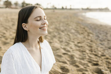 Smiling woman day dreaming while sitting with eyes closed at beach - XLGF02210