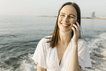 Glückliche Frau, die am Strand mit einem Mobiltelefon spricht - XLGF02214