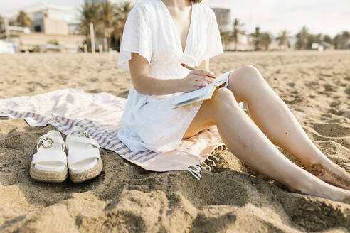 Frau, die am Strand sitzend in ein Buch schreibt - XLGF02215