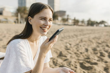 Lächelnde Frau, die am Strand mit ihrem Smartphone telefoniert - XLGF02221