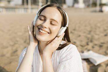 Glückliche Frau hört Musik über Kopfhörer am Strand - XLGF02222