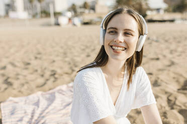 Glückliche junge Frau, die am Strand Musik über drahtlose Kopfhörer hört - XLGF02223