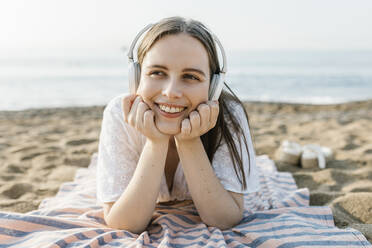 Smiling woman with hands on chin listening music at beach - XLGF02226