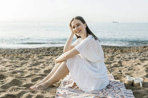 Glückliche schöne Frau sitzt auf Strandtuch - XLGF02230