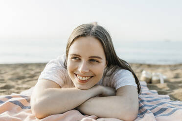 Smiling woman relaxing while lying on beach towel - XLGF02232