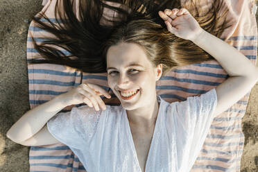 Smiling woman lying on beach towel - XLGF02233