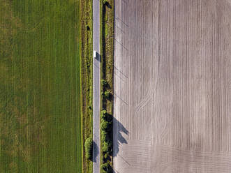 Luftaufnahme eines Busses auf einer Landstraße, die zwei landwirtschaftliche Felder voneinander trennt - KNTF06366