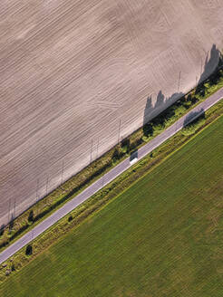 Luftaufnahme eines Busses auf einer Landstraße, die zwei landwirtschaftliche Felder voneinander trennt - KNTF06367