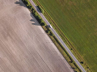Luftaufnahme eines Busses auf einer Landstraße, die zwei landwirtschaftliche Felder voneinander trennt - KNTF06368