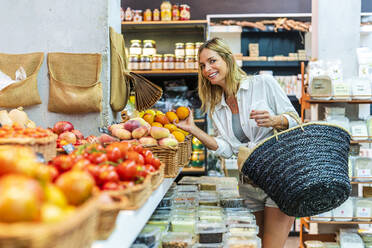 Frau trägt Korb beim Kauf von Obst im Supermarkt - DLTSF02083