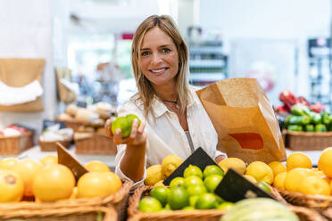 Woman holding limes while shopping in supermarket - DLTSF02084