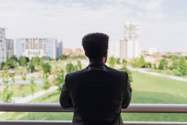 Businessman looking at city view while standing at balcony - MEUF04099