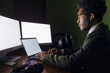 Geschäftsmann mit Mikrofon, der einen Laptop bei der Arbeit im Heimbüro benutzt - MEUF04114