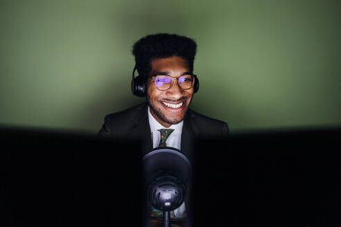 Smiling male professional with headphones live streaming at home - MEUF04119