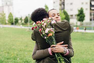 Geschäftsfrau hält Blumenstrauß und umarmt Kollegen im Park - MEUF04122