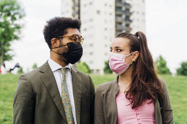Business couple with protective face masks looking at each other - MEUF04123
