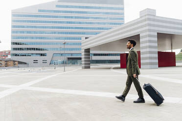 Businessman with wheeled luggage walking on footpath - MEUF04127