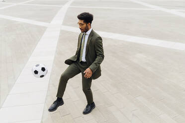 Businessman playing with soccer ball on footpath - MEUF04131