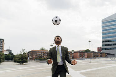 Businessman heading the ball while playing in city - MEUF04136