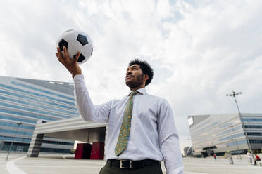 Businessman holding soccer ball while standing in city - MEUF04143