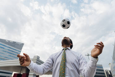 Geschäftsmann köpft den Ball beim Spielen in der Stadt - MEUF04144