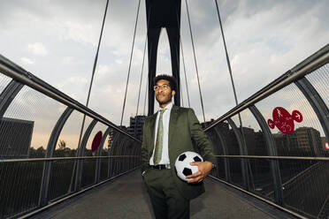 Geschäftsmann mit Fußball stehend auf Brücke bei Sonnenuntergang - MEUF04156