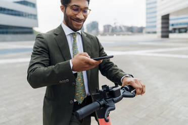 Smiling businessman unlocking electric push scooter through mobile phone - MEUF04157