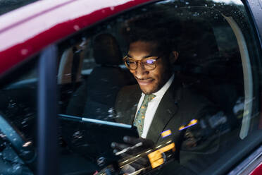 Lächelnder Geschäftsmann, der ein digitales Tablet benutzt, während er im Auto sitzt - MEUF04162